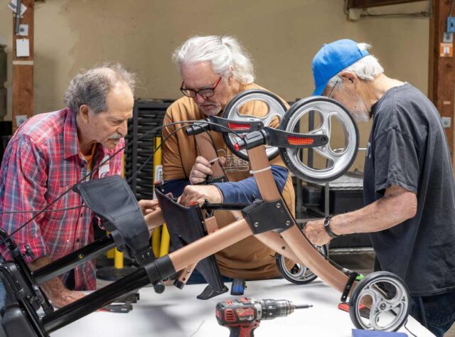 Three men work together to repair a wheelchair at a Grey Bears Repair Cafe