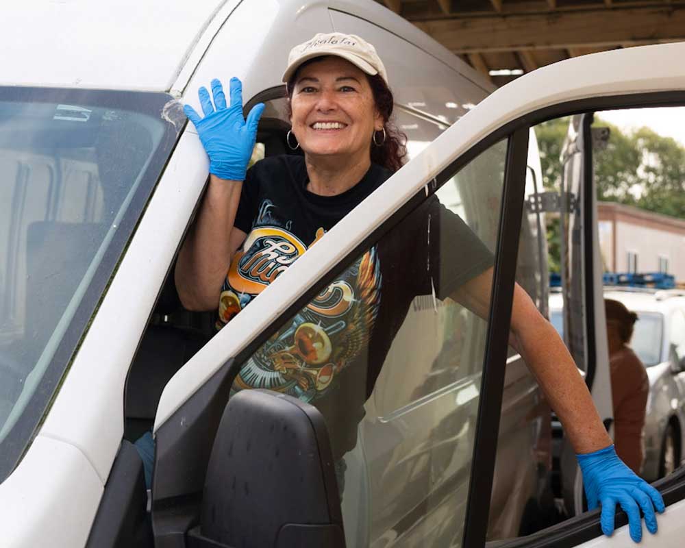 Smiling food distribution volunteer waves from truck
